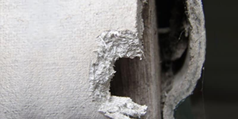 Deteriorating asbestos pipe insulation exposed inside a wall